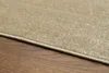 A close-up view of the edge of a beige rug on a wooden floor. Produktbild-Vorschau