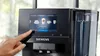 A hand is touching the screen of a Siemens coffee machine, selecting a drink. Produktbild-Vorschau