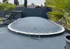 An oval inflatable pool cover is shown in a backyard setting, surrounded by paving stones and greenery. Produktbild-Vorschau