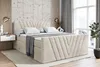 A bedroom scene featuring a taupe velvet boxspring bed with a headboard and footboard, complete with pillows and a throw blanket. The room has a modern aesthetic with textured walls, wooden accents, and a large window with curtains. Produktbild-Vorschau