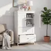 A white storage cabinet with two doors and two drawers, shown in a room setting with a sofa and a plant. Produktbild-Vorschau