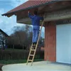A person is using a wooden ladder to access the roof of a brick building. Produktbild-Vorschau