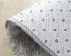 The underside of a gray shaggy rug is shown, with a patterned backing and a rolled edge. The rug is placed on a wooden floor. Náhled obrázku produktu