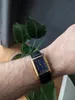 A person's wrist wearing a gold-cased watch with a blue face and a black leather strap. Produktbild-Vorschau