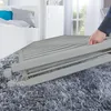 A person's hand is shown folding a baby crib on a fluffy gray carpet. Produktbild-Vorschau