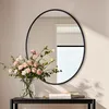 A round mirror with a black frame hangs on a wall above a console table with a vase of pink flowers and some books. Podgląd zdjęcia produktu