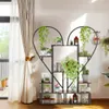 A heart-shaped plant stand filled with various plants and books, placed indoors near a window with curtains. Produktbild-Vorschau