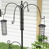 A black metal bird feeder station with two feeders hanging from it, set against a white clapboard wall and green grass. Voir les images du produit
