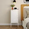A white metal nightstand with a closed door and a vent detail on the lower part of the door, placed next to a bed. Anteprima dell’immagine prodotto