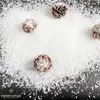 Pinecones dusted with artificial snow are arranged on a dark surface, with a scattering of snow around them. A logo and text are in the bottom left corner. Náhled obrázku produktu