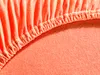 A close-up view of the elasticized edge of an orange jersey fitted sheet. Produktbild-Vorschau