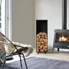 A cozy living room scene with a fireplace, firewood storage, and a chair. Produktbild-Vorschau