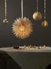 A festive scene with a paper star lantern and golden baubles hanging above a table set with a linen tablecloth, a bowl of nuts, and fairy lights. Podgląd zdjęcia produktu