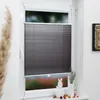 A dark gray pleated blind is installed on a white window frame, partially covering the window. Decorative items are placed on the windowsill below. Produktbild-Vorschau