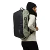 A person wearing a black beanie and a light-colored long-sleeved shirt is shown from the side, wearing a large duffel bag/backpack on their back. The bag is black and light green, with the "Jack Wolfskin" logo visible on the green section. Produktbild-Vorschau