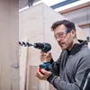 A man is using a cordless drill to drill a hole in a wooden structure. Voir les images du produit