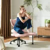A woman is sitting on a pink ergonomic meditation chair in a room with curtains and a plant. Produktbild-Vorschau