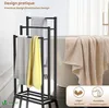 A black metal towel rack with three bars is shown in a bathroom setting, holding white, yellow, and beige towels. A bathtub is visible in the background. Produktbild-Vorschau