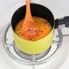 A close-up shot of a small, light yellow saucepan with a wooden spoon stirring a bright orange liquid with seeds inside. The saucepan is placed on a stove grate. Náhled obrázku produktu
