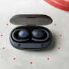 A pair of black wireless earbuds in an open charging case, placed on a textured light gray surface with red dots scattered around. Produktbild-Vorschau