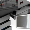 A close-up view of a modern vanity table with drawers and a lighted mirror, featuring makeup and accessories. Produktbild-Vorschau