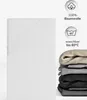 A white fitted sheet is shown folded on the left, and a stack of folded fitted sheets in various colors (beige, gray, black) is shown on the right. Icons and text indicating material and washing instructions are also present. Produktbild-Vorschau