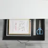An open drawer containing a framed picture, a ruler, and scissors. Anteprima dell’immagine prodotto