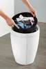 Hands placing a black laundry bag filled with clothes into a white laundry hamper. Náhľad obrázku produktu