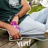 A person sitting on a wooden bench outdoors, holding a package of VIVIL Schwarze Johannisbeere Hustenbonbons. Produktbild-Vorschau