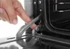 A close-up view of a person's finger interacting with a metal latch on an oven door. Produktbild-Vorschau