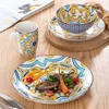 A table setting with a plate of food, a mug, and a bowl on a saucer, all decorated with a colorful bohemian pattern. Náhled obrázku produktu