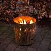 A fire pit with flames burning inside, placed on a paved patio with autumn leaves in the background. Produktbild-Vorschau