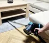 A person is vacuuming a rug under a coffee table with a cordless vacuum cleaner. Podgląd zdjęcia produktu