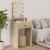 A makeup vanity with a mirror and lights, a stool, and a large plant next to it, with a bed in the background. Voir les images du produit