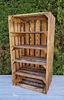 A wooden crate shelf unit is displayed outdoors against a green hedge and a gray surface. Náhled obrázku produktu