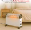 An electric heater is placed on a carpeted floor next to a bedside table and a bed in a bedroom. Produktbild-Vorschau