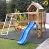 A wooden playground set with a slide, swing, and climbing net, set up outdoors on a rubber mat and grass. Náhľad obrázku produktu