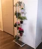 A white metal plant stand with several potted plants on a wooden floor next to a white wall and closet doors. Náhľad obrázku produktu