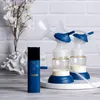 A double electric breast pump with its control unit, placed on a white circular stand, with a decorative white coral and a vase of white flowers in the background. Podgląd zdjęcia produktu