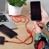 A person is charging multiple phones and a laptop with a red USB cable. Anteprima dell’immagine prodotto