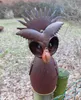 A rusty metal owl garden decoration is mounted on a wooden post in an outdoor setting with dry leaves on the ground. Produktbild-Vorschau