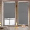 A bedroom scene with two windows covered by dark gray pleated blinds. The blinds are partially open, revealing a snowy outdoor view. Decorative candles and lights are placed on the windowsill. Produktbild-Vorschau