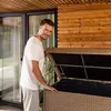 A man is standing next to an open storage box on a patio. Produktbild-Vorschau