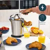 A person is using a juicer to make orange juice, with breakfast items like croissants and strawberries on the table. Produktbild-Vorschau