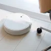 A white robot vacuum cleaner is on a light-colored wooden floor, next to a chair leg with a wheel. Anteprima dell’immagine prodotto