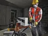 A construction worker is using a specialized saw to cut a block of material on a sawhorse. A vacuum cleaner is visible in the background. Náhľad obrázku produktu