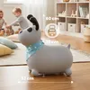 Two children are playing in a room with a grey dog-shaped bouncing toy. The toy has a blue bandana with white stars around its neck. There are shelves in the background with baskets and books. The floor is wooden. Produktbild-Vorschau