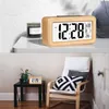 A digital alarm clock is shown on a shelf next to a candle, and another smaller digital alarm clock is shown on a side table next to a chair. Produktbild-Vorschau