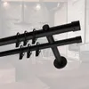 A close-up view of a black double curtain rod with rings, set against a blurred interior background. Produktbild-Vorschau