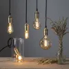 Several decorative Edison-style LED light bulbs with spiral filaments are displayed against a plain gray background. One bulb is placed inside a clear glass jar on a wooden surface, and a small bouquet of dried grasses in a glass vase is visible on the rig Podgląd zdjęcia produktu